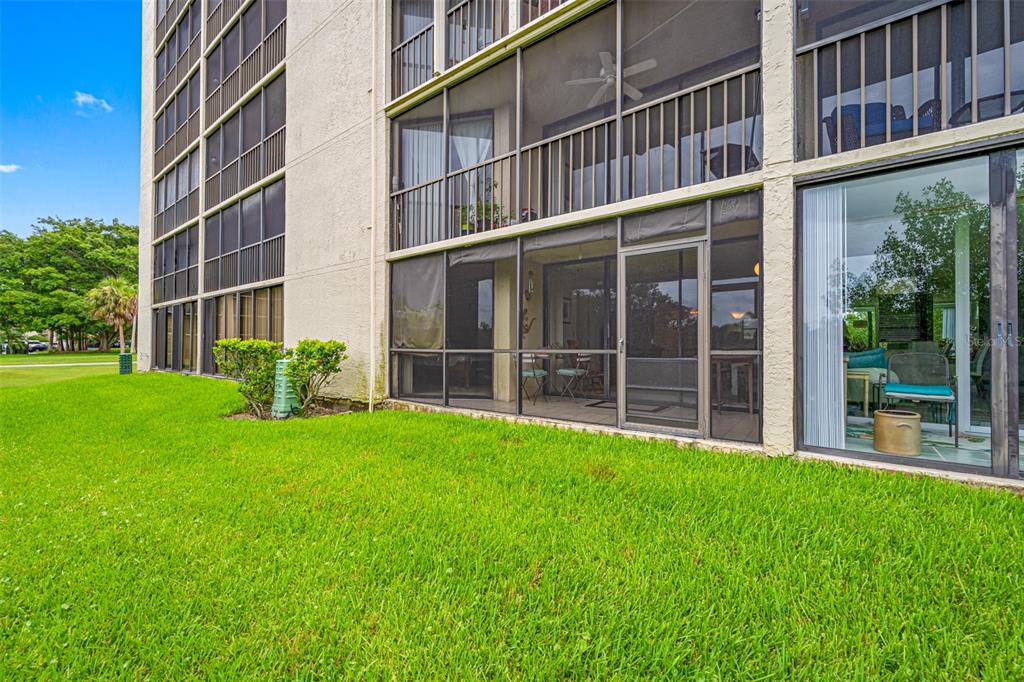 The exterior of a multi-story apartment building features ground-floor screened lanais and green grass — 900 COVE CAY DRIVE UNIT 1F, CLEARWATER, FL