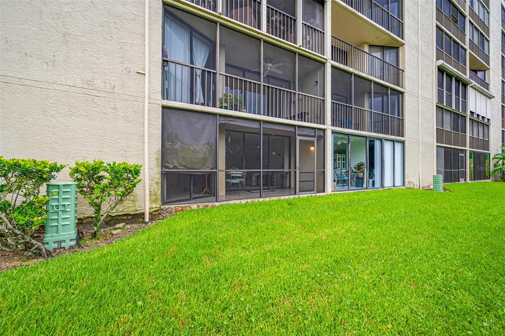 A ground-level view of a multi-story apartment building with screened-in patios and green lawn — 900 COVE CAY DRIVE UNIT 1F, CLEARWATER, FL