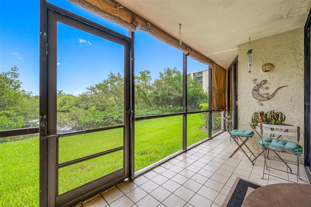 A screened-in porch with tiled flooring overlooks a grassy lawn and dense green trees — 900 COVE CAY DRIVE UNIT 1F, CLEARWATER, FL