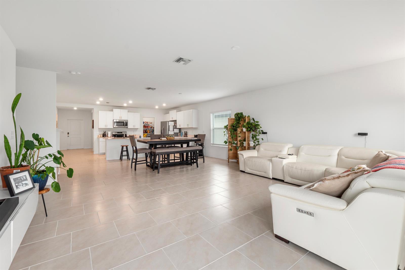 An open-concept living room and kitchen featuring white cabinetry, tile flooring, and a white sectional — 17177 Monte Isola Way, FL 33917, FL