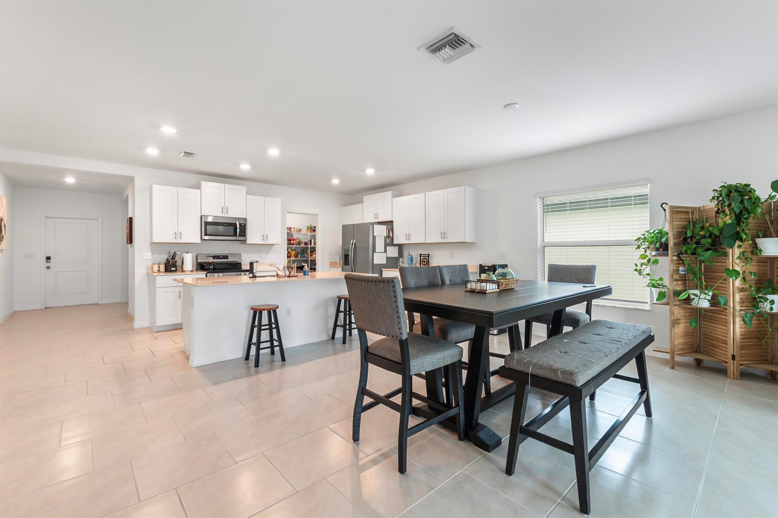 A bright open-concept kitchen and dining area features white cabinetry, tile flooring, and dark furniture — 17177 Monte Isola Way, FL 33917, FL