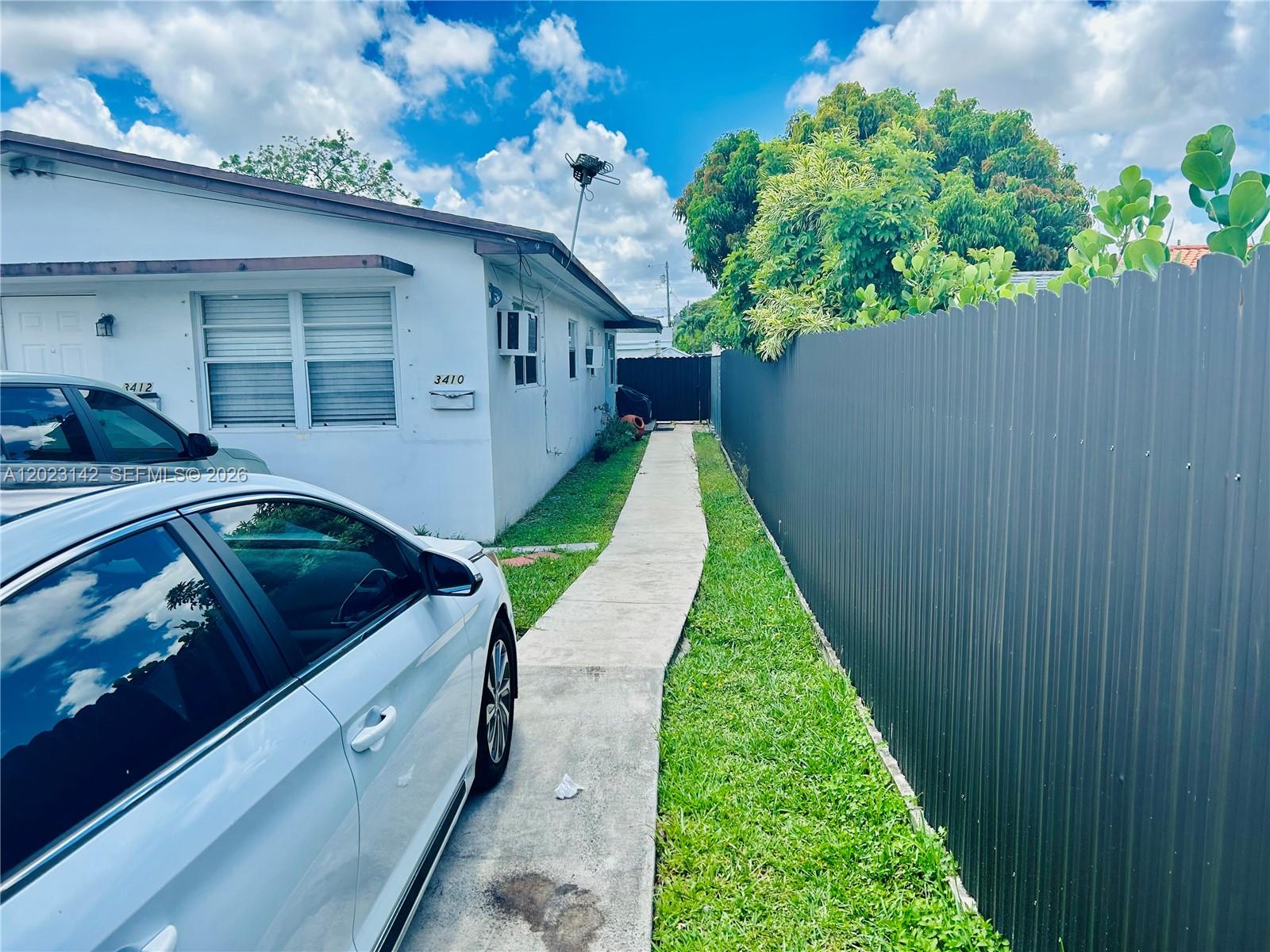A white house with a concrete walkway sits beside a tall gray metal fence — 3410 SW 89th Ct, Miami FL 33165, MIAMI, FL