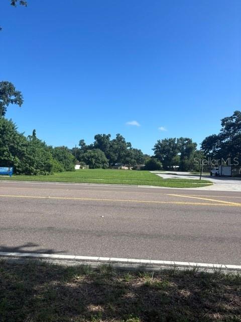 A vacant, grassy lot sits across a paved road under a clear blue sky — 54TH AVENUE N, KENNETH CITY, FL