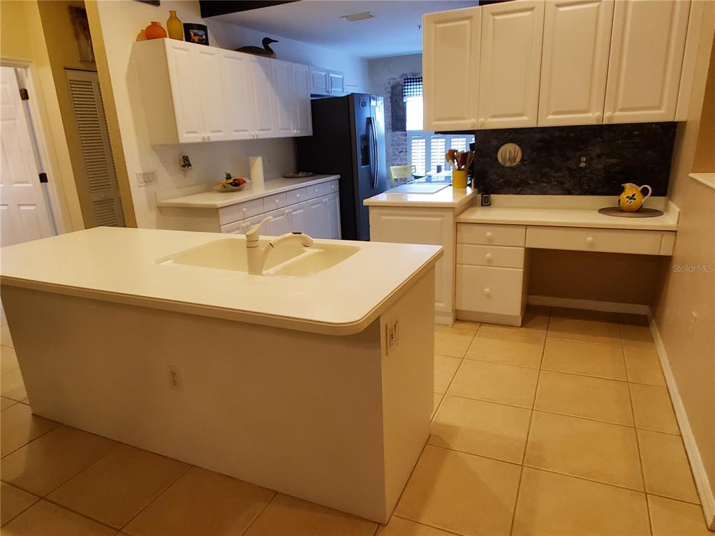 A kitchen features white cabinets, a central island with a sink, and light-colored tile flooring — 7138 CEDAR HOLLOW CIRCLE, BRADENTON, FL