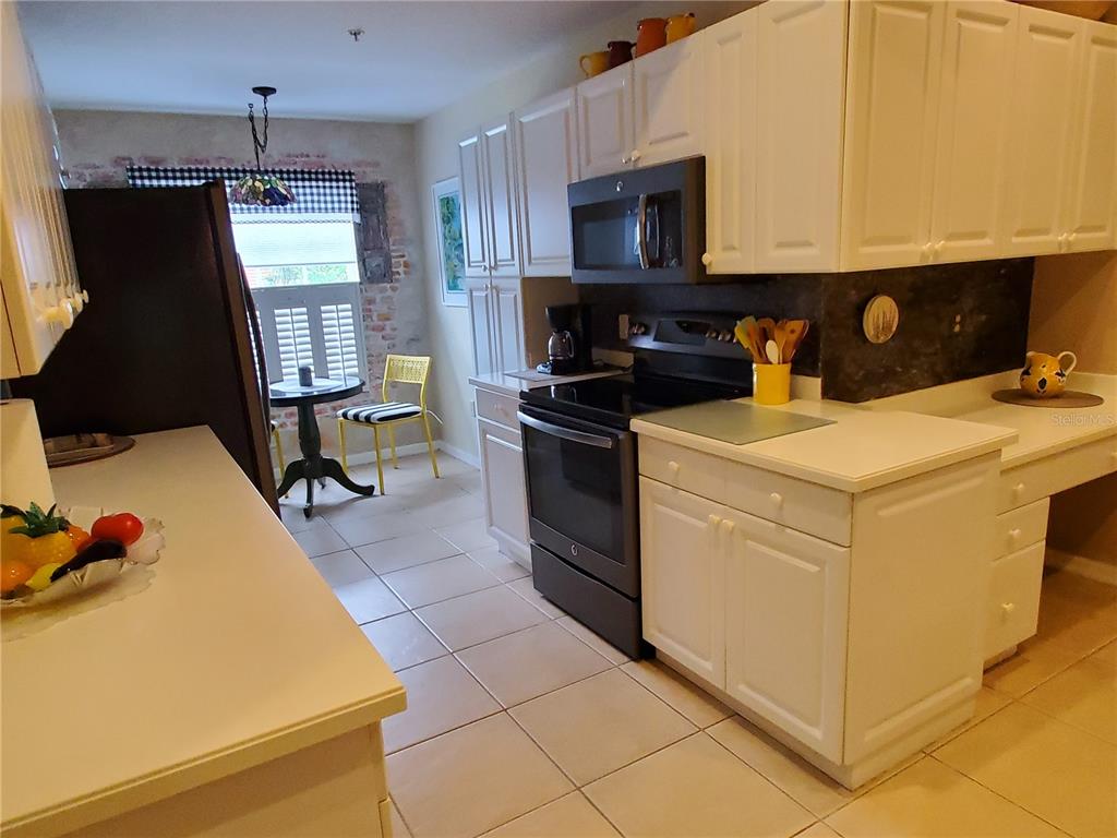 A kitchen features white cabinets, black appliances, tile flooring, and a small dining area — 7138 CEDAR HOLLOW CIRCLE, BRADENTON, FL