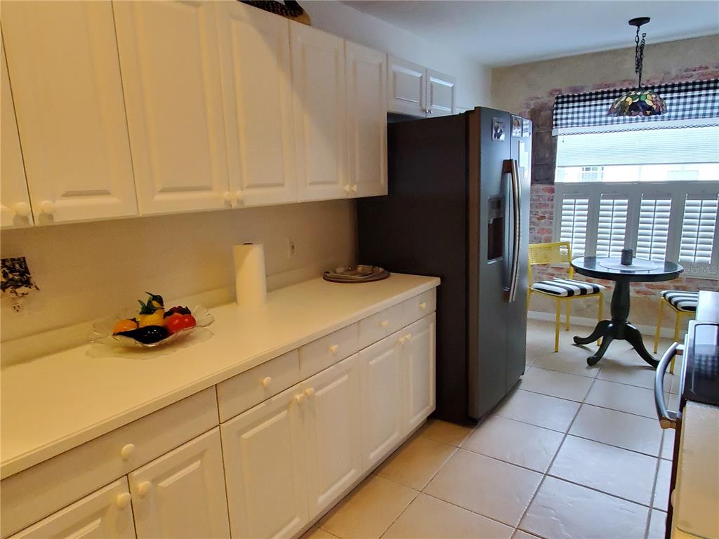 A kitchen features white cabinets, a black refrigerator, and a small dining area with shutters — 7138 CEDAR HOLLOW CIRCLE, BRADENTON, FL
