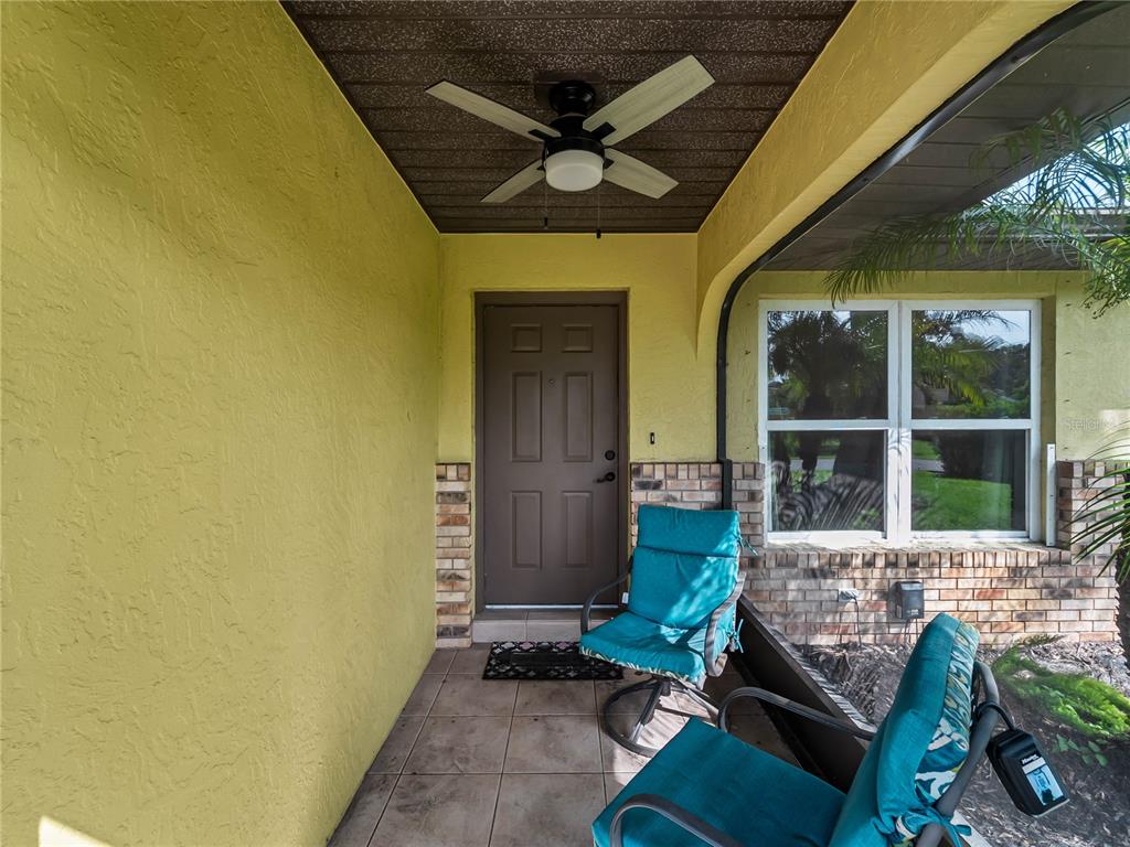 A covered front porch features a brown door, tiled floor, ceiling fan, and two chairs — 251 PLANTATION ROAD, VENICE, FL