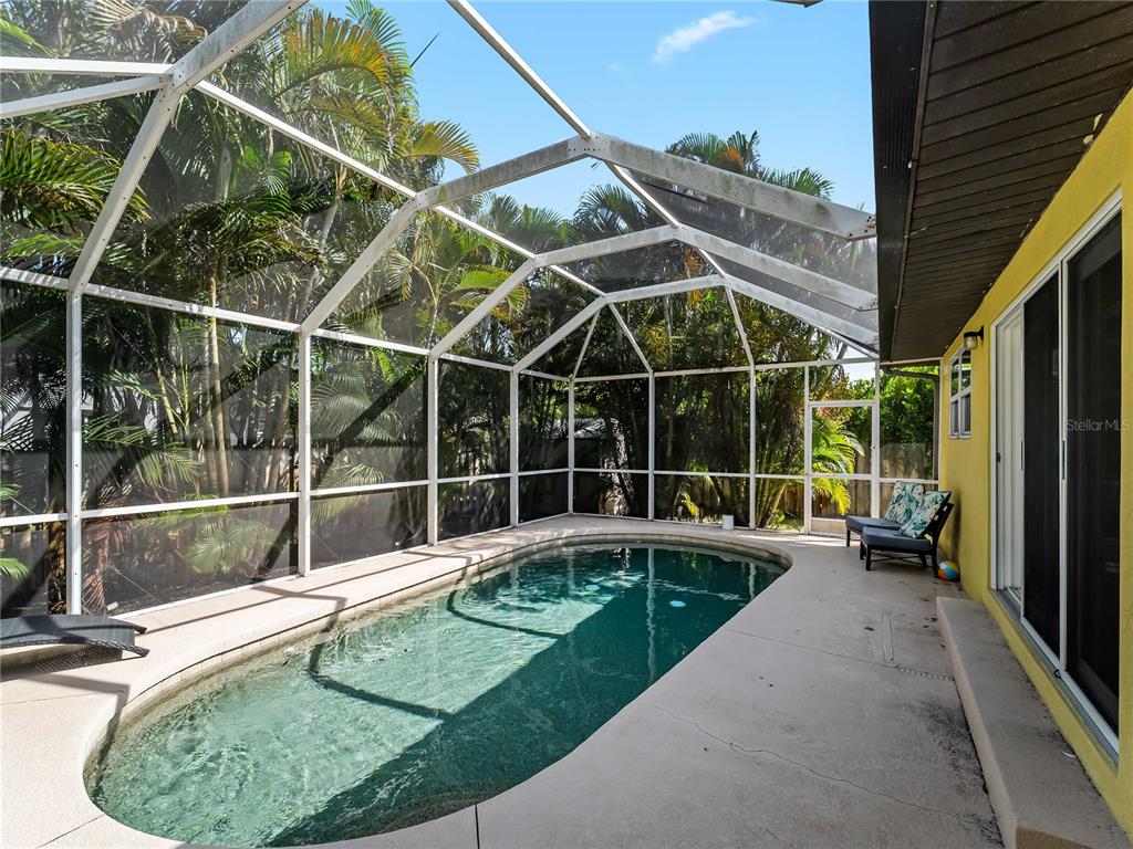 A screened-in swimming pool sits on a concrete patio next to a yellow house — 251 PLANTATION ROAD, VENICE, FL
