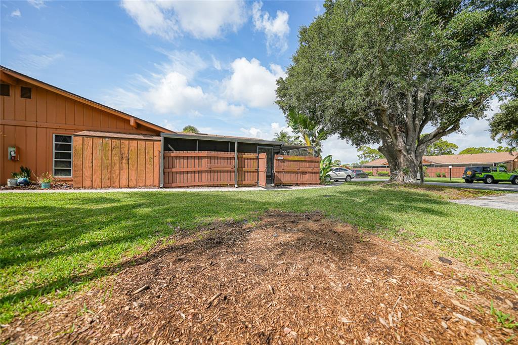 An exterior view of a house with wood siding, a fenced patio, and a large tree — 5625 FOXLAKE DRIVE, NORTH FORT MYERS, FL