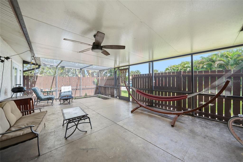 A screened-in concrete patio features a ceiling fan, a hammock, and outdoor furniture — 5625 FOXLAKE DRIVE, NORTH FORT MYERS, FL