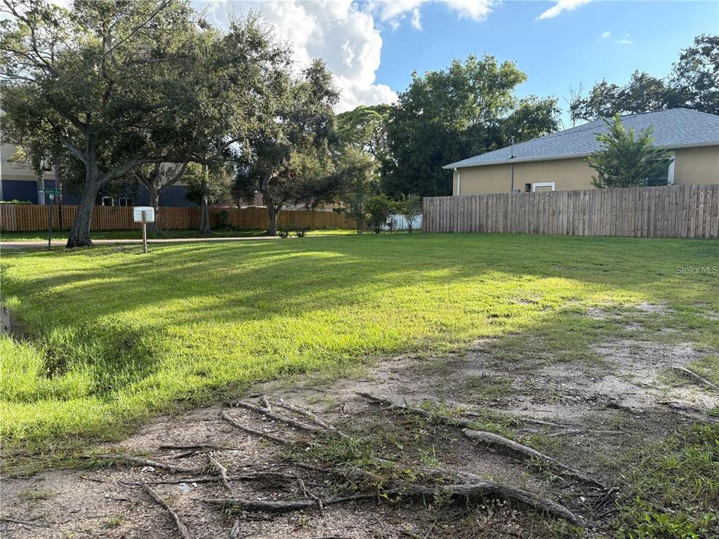 A grassy vacant lot features mature trees and a wooden privacy fence — 3215 LAUREL AVENUE, CLEARWATER, FL