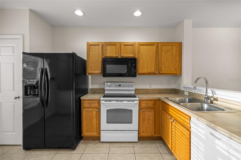 A kitchen features wood cabinets, a black refrigerator, a white stove, and a double sink — 4428 SW 49TH AVENUE, OCALA, FL