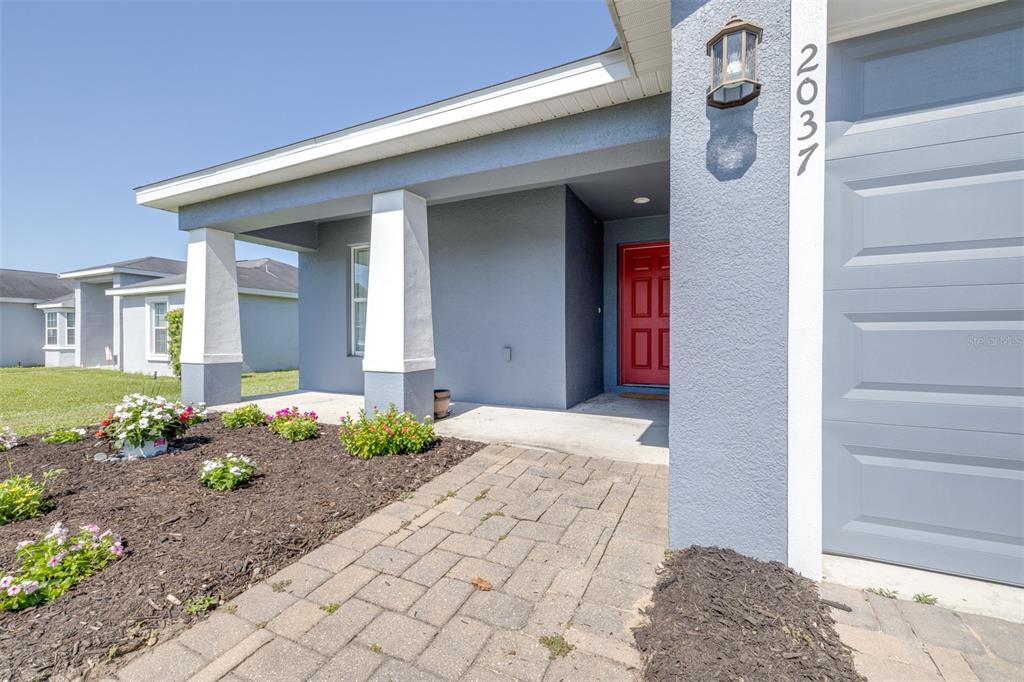 A blue stucco house exterior features a red front door and a paved walkway — 2037 CHARLESTON LANE, BARTOW, FL