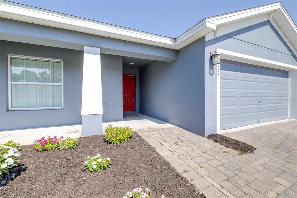 A blue house exterior features a red front door, a garage, and a landscaped garden — 2037 CHARLESTON LANE, BARTOW, FL