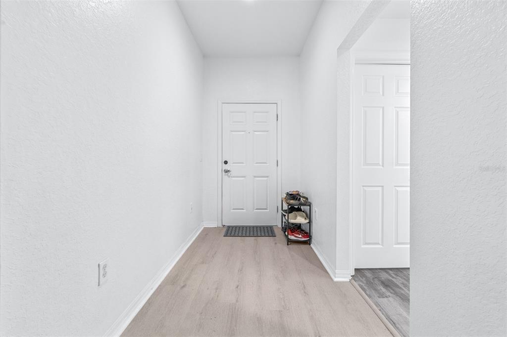An entryway features light wood-look flooring, white walls, a white front door, and a shoe rack — 2037 CHARLESTON LANE, BARTOW, FL