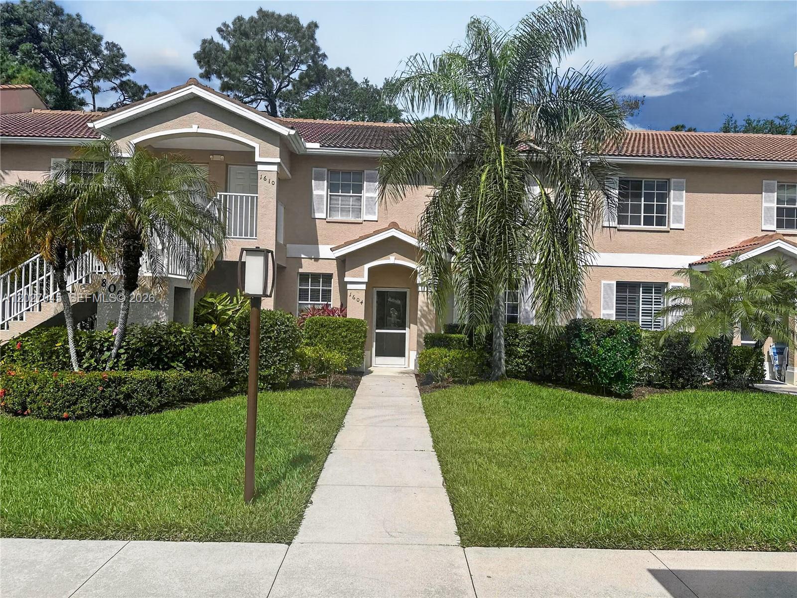 A two-story tan stucco townhouse with a palm tree and a concrete walkway — NAPLES, FL