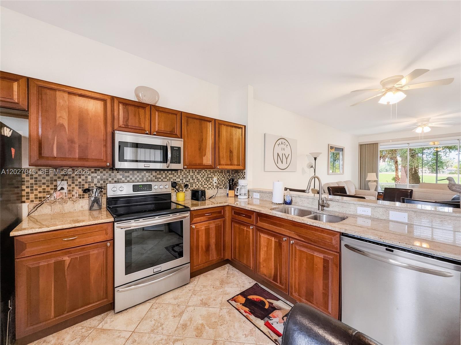 A kitchen features wood cabinets, granite countertops, stainless steel appliances, and a tile floor — NAPLES, FL