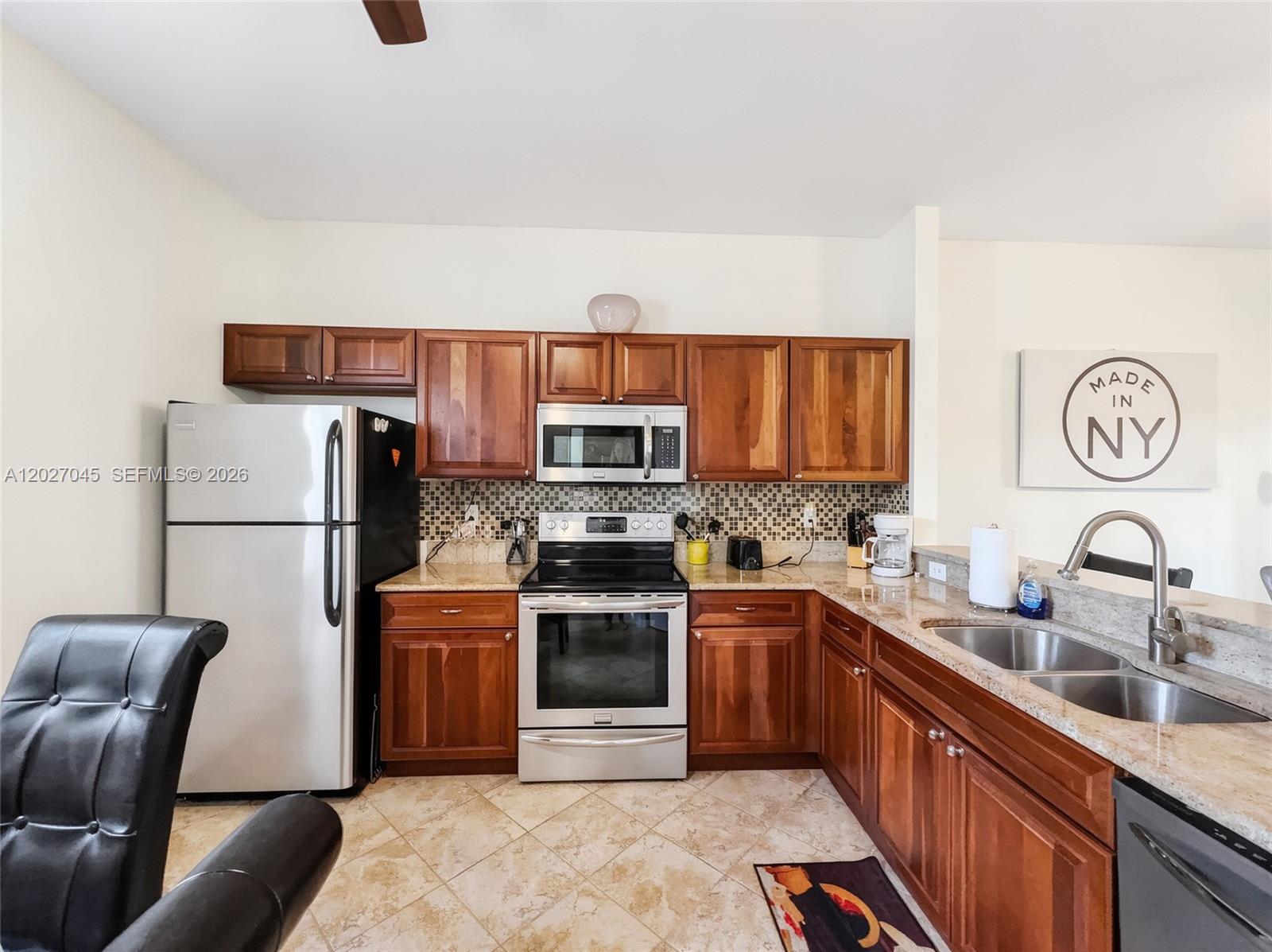 A kitchen features wooden cabinets, stainless steel appliances, granite countertops, and a tiled floor — NAPLES, FL