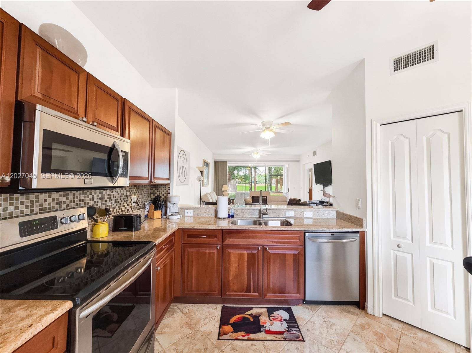 A kitchen with wood cabinets, stainless steel appliances, and tile flooring overlooks a living area — NAPLES, FL