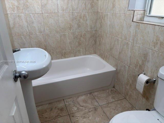 A bathroom features a pedestal sink, a white bathtub, and beige tiled walls and floors — 2059 SW 7th St # 0, Miami FL 33135, MIAMI, FL