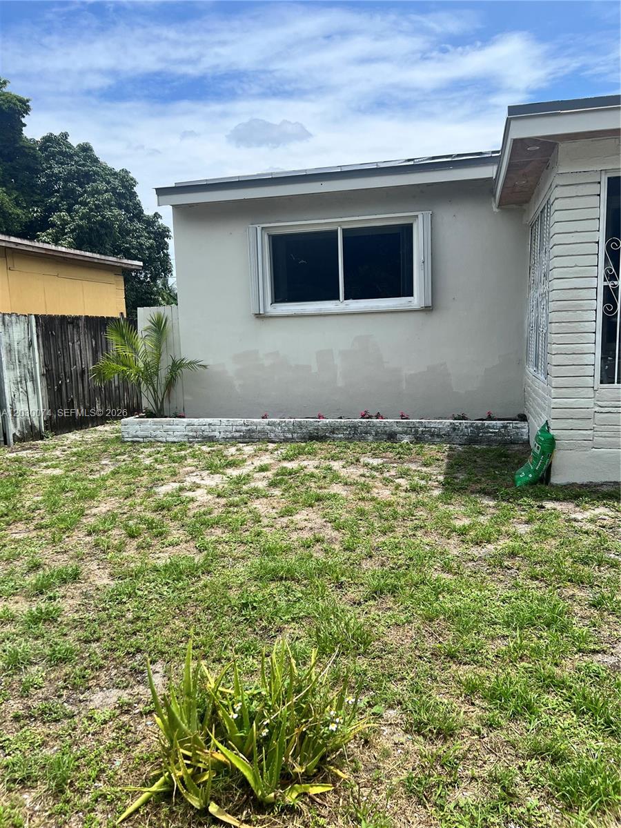 A view of a backyard featuring a small palm tree, a low stone planter, and grass — 250 NE 160th St, Miami FL 33162, MIAMI, FL
