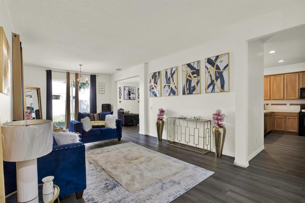 A living room with blue furniture, a patterned rug, and wall art on a white wall — 7224 LUMBER PORT DRIVE, SUN CITY CENTER, FL
