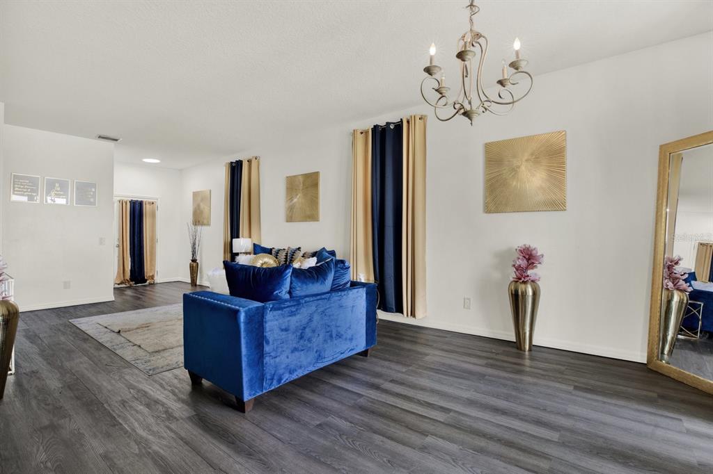 A living room features a blue velvet sofa, dark wood flooring, and gold-toned wall art — 7224 LUMBER PORT DRIVE, SUN CITY CENTER, FL