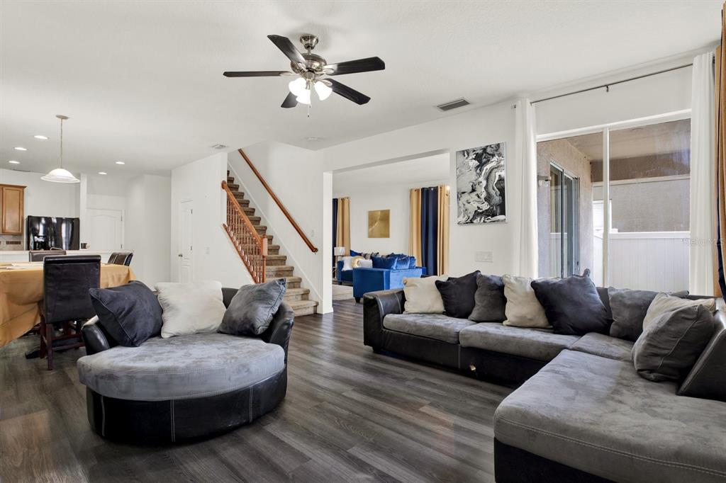 A living room with dark wood-look flooring, a sectional sofa, a round chair, and stairs — 7224 LUMBER PORT DRIVE, SUN CITY CENTER, FL