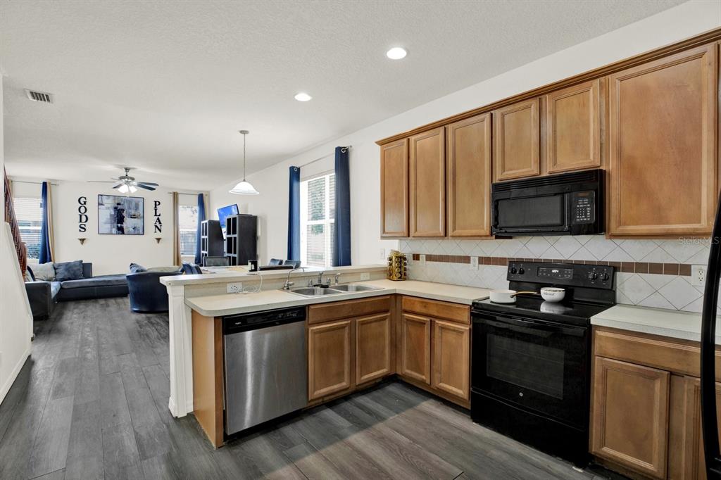 A kitchen with wood cabinets and stainless steel appliances overlooks an open-concept living area — 7224 LUMBER PORT DRIVE, SUN CITY CENTER, FL
