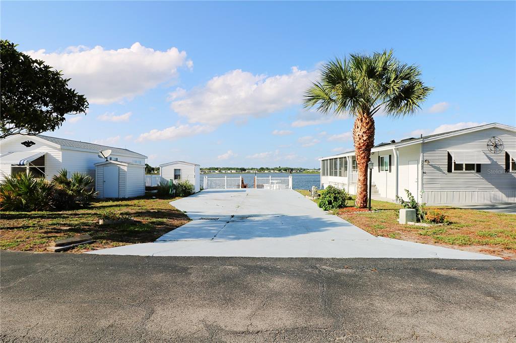 A mobile home with a palm tree and a concrete driveway facing a lake — 7205 WINDSONG DRIVE, LAKE WALES, FL