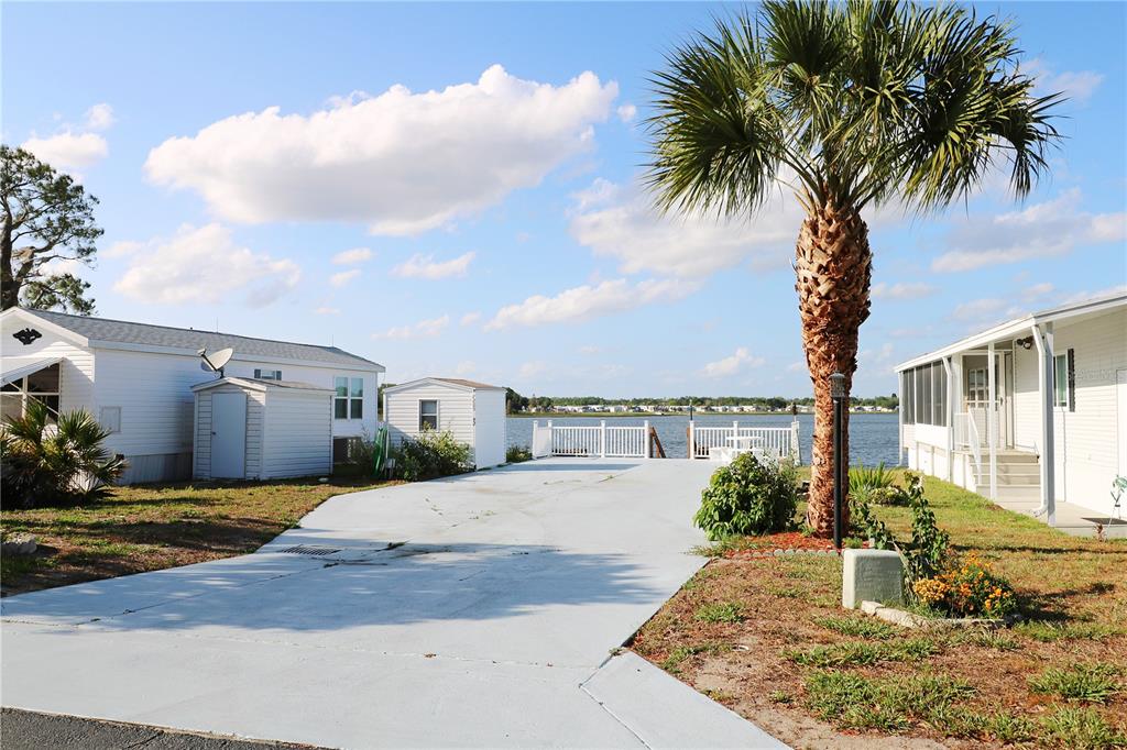 A paved driveway sits between two mobile homes, leading to a white fence overlooking water — 7205 WINDSONG DRIVE, LAKE WALES, FL