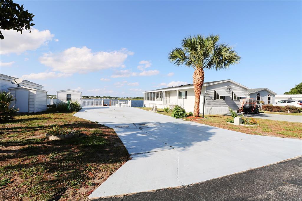 A paved driveway leads to a waterfront view between two mobile homes and a palm tree — 7205 WINDSONG DRIVE, LAKE WALES, FL