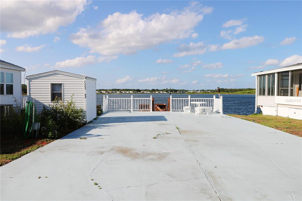 A concrete patio sits between two mobile homes, featuring a white railing overlooking a lake — 7205 WINDSONG DRIVE, LAKE WALES, FL