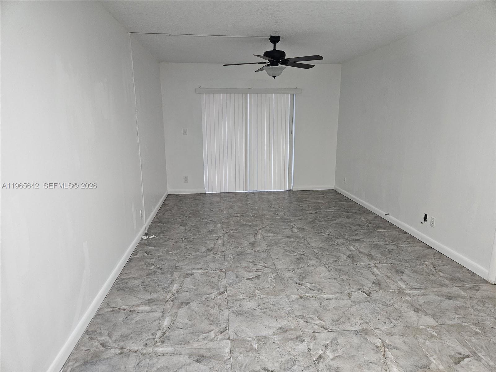An empty room features white walls, a ceiling fan, and gray marble-patterned tile flooring — 7610 Stirling Rd # 102C, Davie FL 33024, DAVIE, FL