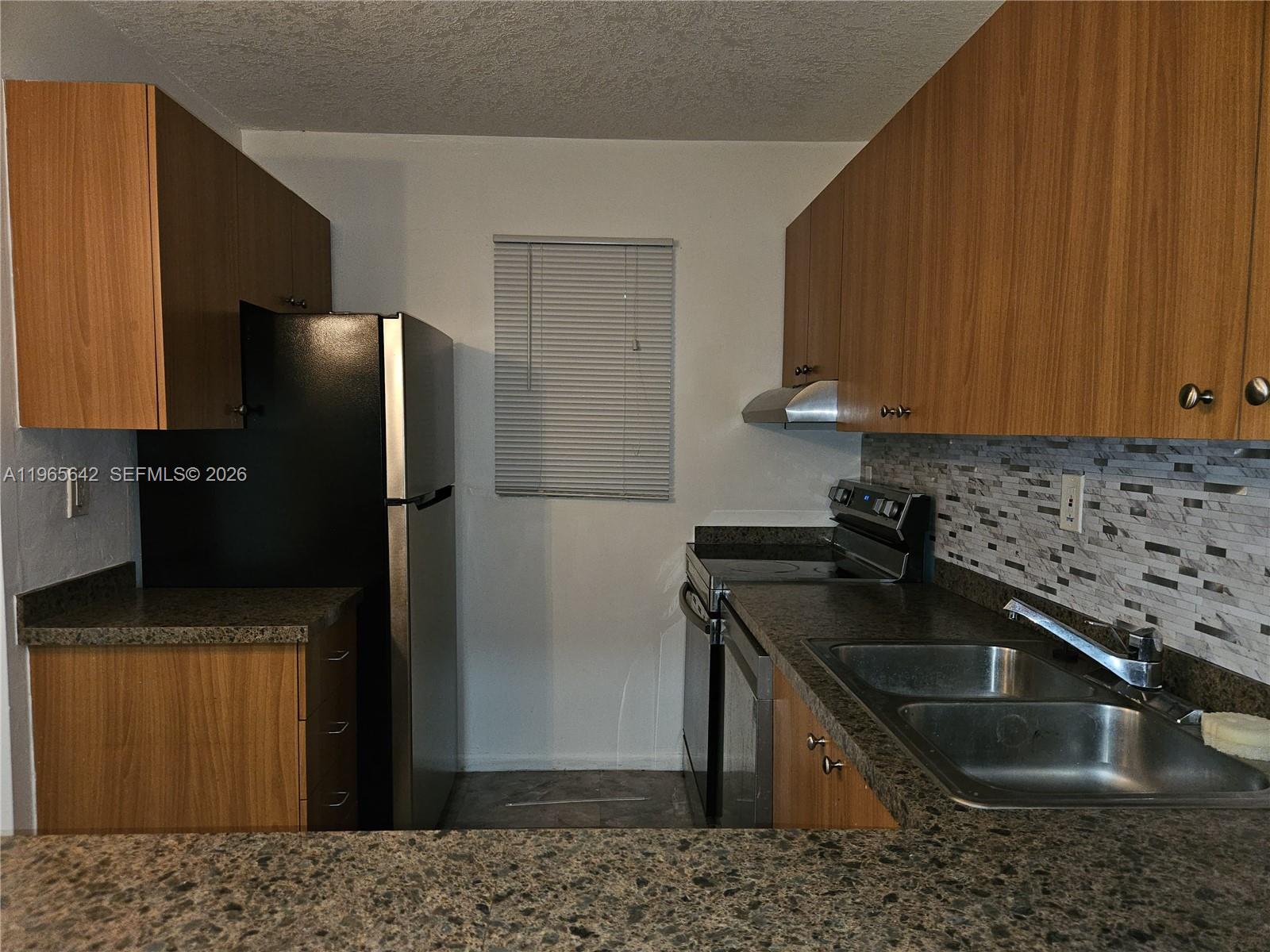 A kitchen features wood cabinets, granite countertops, a stainless steel refrigerator, and a double sink — 7610 Stirling Rd # 102C, Davie FL 33024, DAVIE, FL