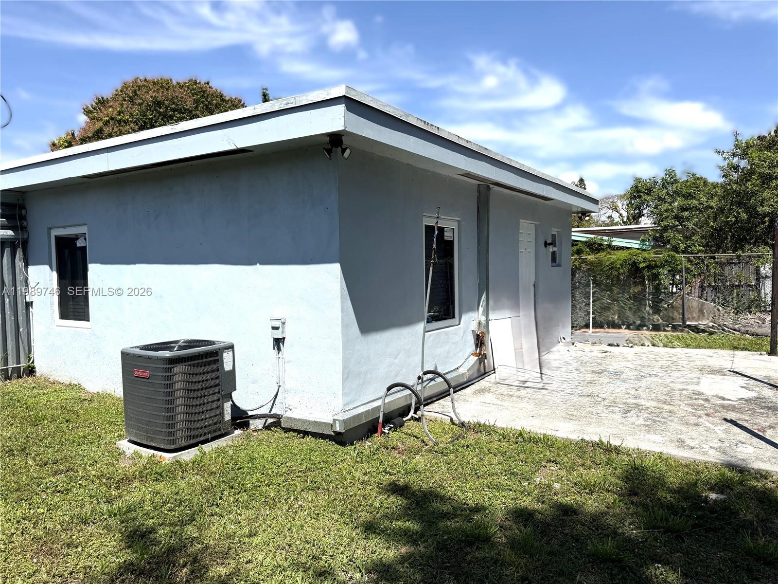 The exterior of a light blue, flat-roofed building features an air conditioning unit and patio — 9615 NW 26th Ave, Miami FL 33147, MIAMI, FL