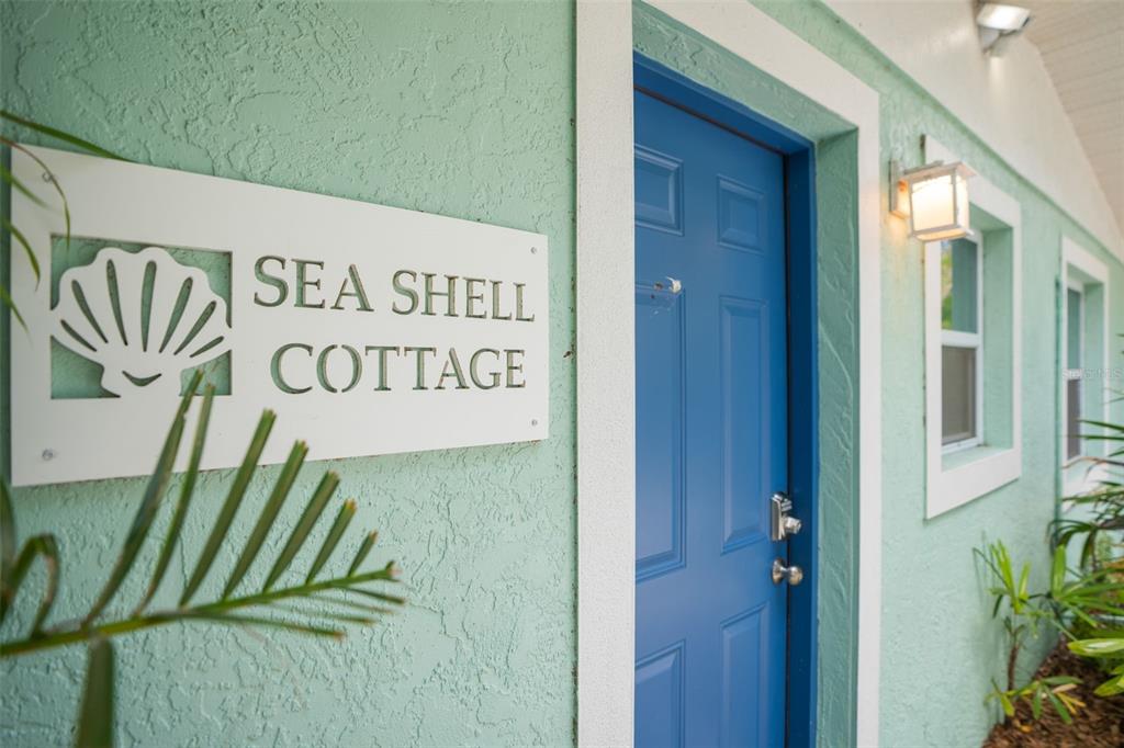 A teal exterior wall features a Sea Shell Cottage sign and a blue entry door — 2053 ROSELAWN STREET, SARASOTA, FL