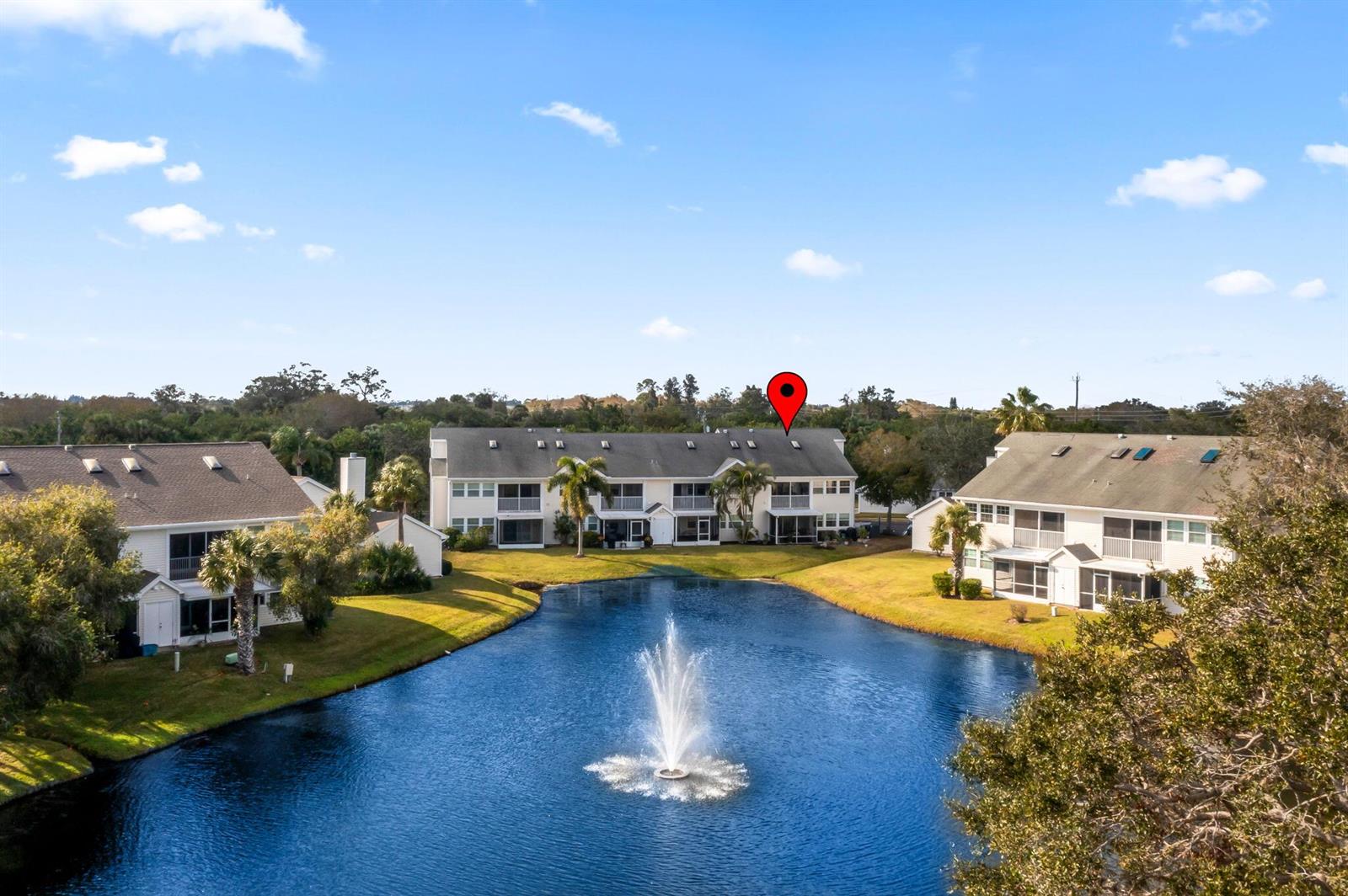An aerial view shows multi-story apartment buildings surrounding a pond with a central fountain — 1940 Westminster Circle # 1, Vero Beach FL 32966, VERO BEACH, FL