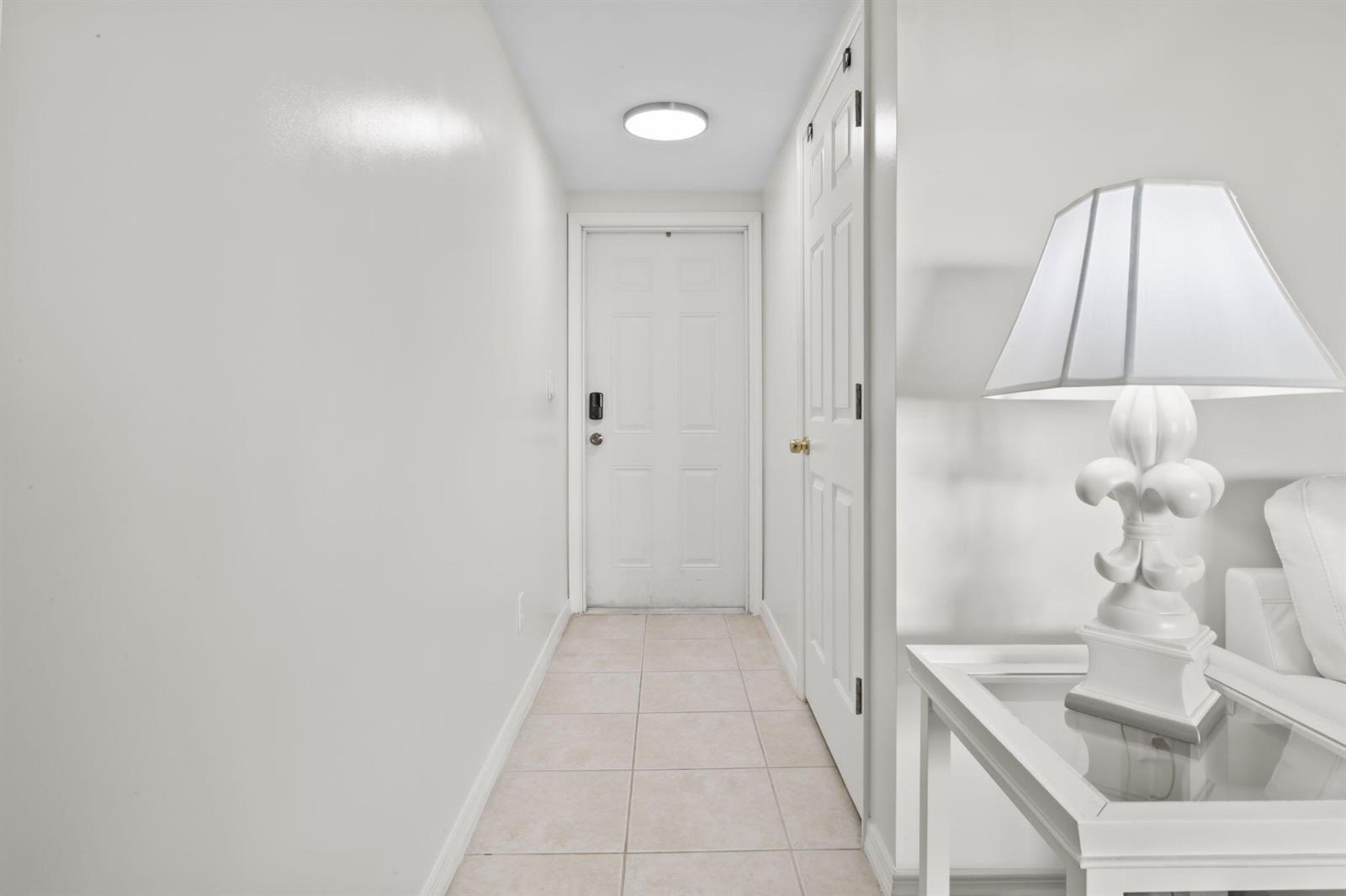 A white hallway features tiled flooring, a flush-mount ceiling light, and two white doors — 1940 Westminster Circle # 1, Vero Beach FL 32966, VERO BEACH, FL