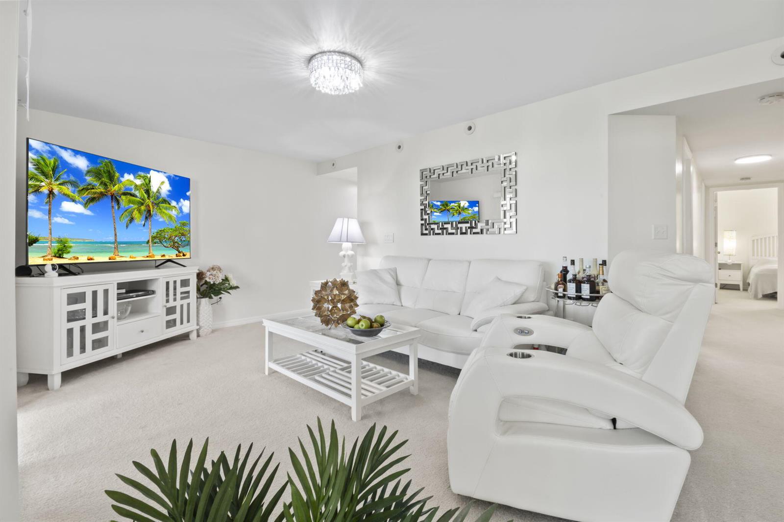 A bright living room features white furniture, a large television, and a crystal ceiling light — 1940 Westminster Circle # 1, Vero Beach FL 32966, VERO BEACH, FL