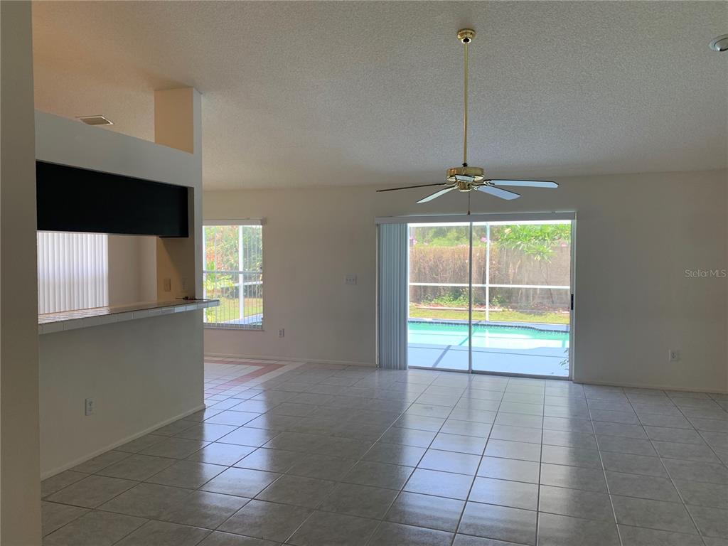 A tiled living room features a ceiling fan, a breakfast bar, and sliding glass doors — 11417 GLENMONT DRIVE, TAMPA, FL