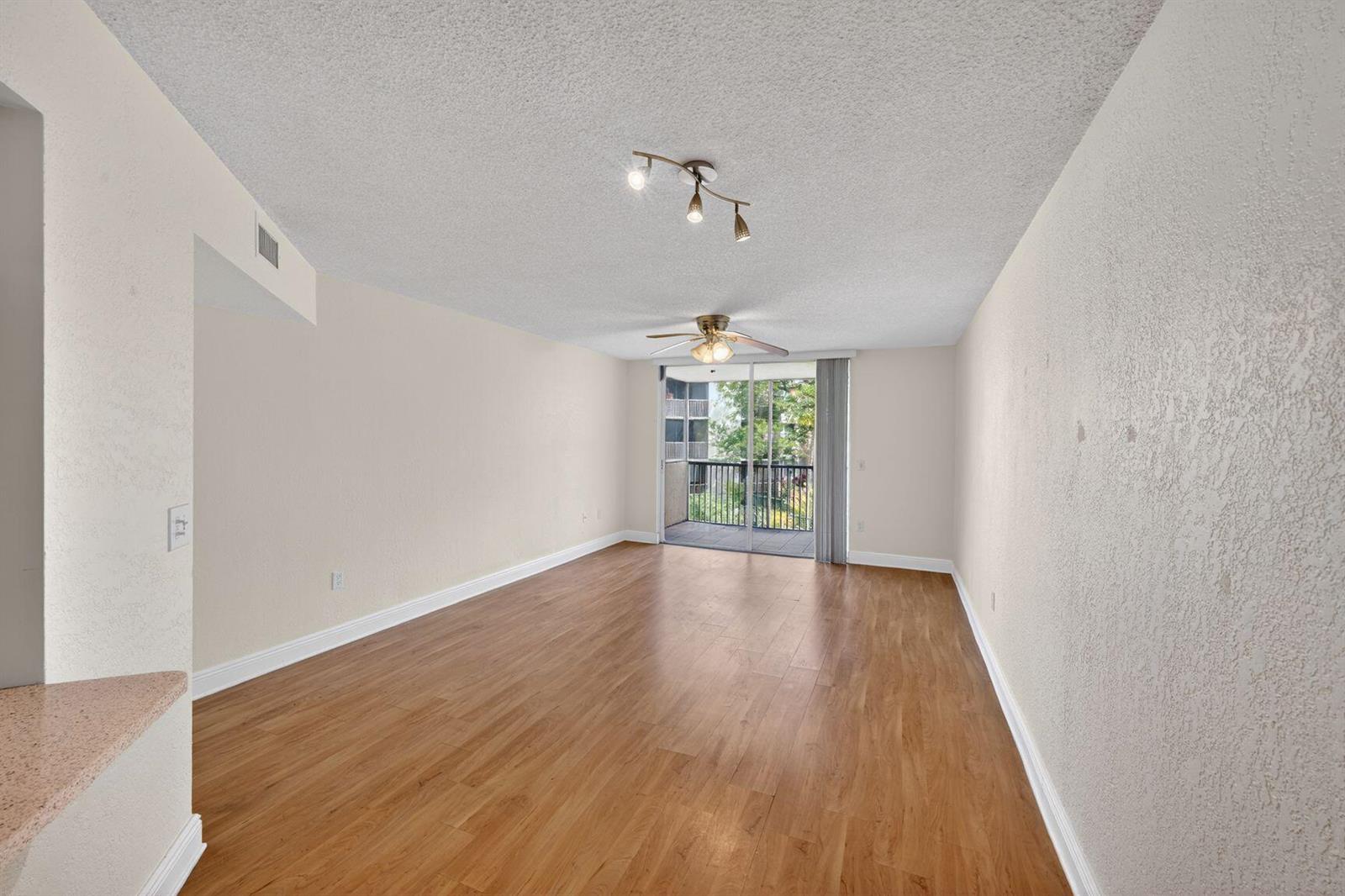 An empty living room with wood-look flooring, a ceiling fan, and a sliding glass door — 8353 Lake Drive # 204, Doral FL 33166, DORAL, FL