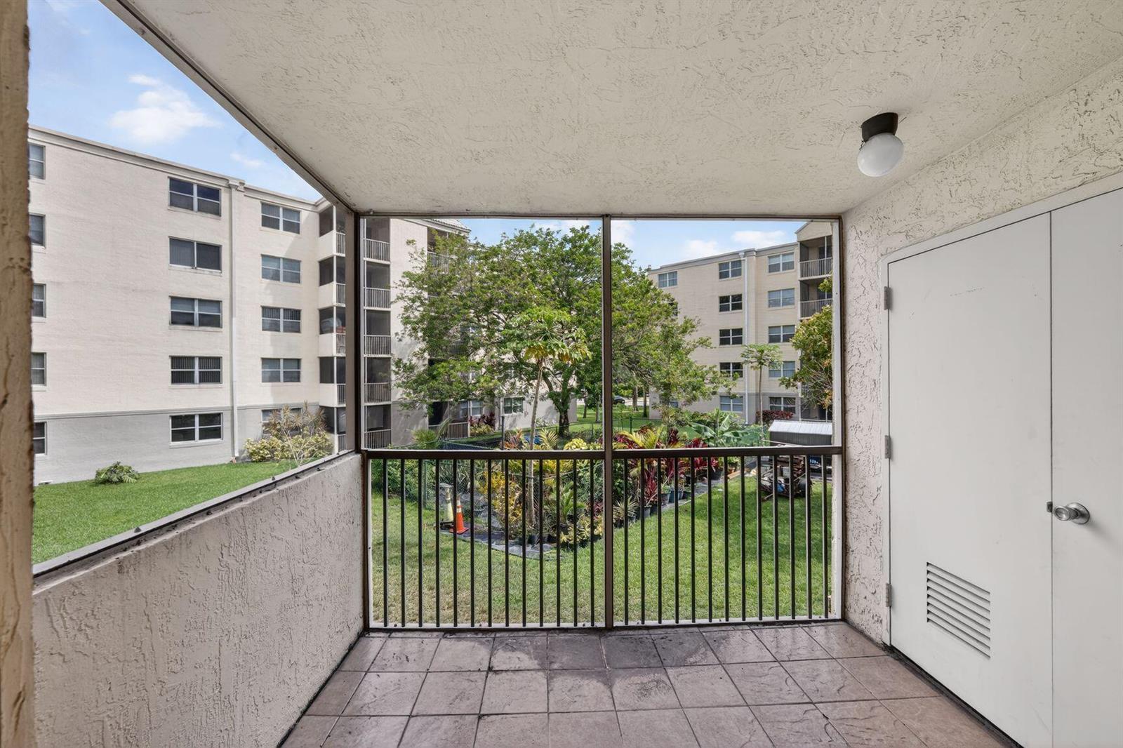 A screened-in balcony with tiled flooring overlooks a grassy courtyard between two apartment buildings — 8353 Lake Drive # 204, Doral FL 33166, DORAL, FL
