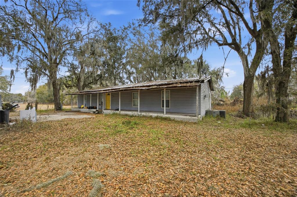 A single-story house with gray siding and a front porch sits on a leaf-covered lot — 1823 WELCOME ROAD, LITHIA, FL