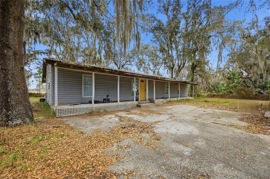 A single-story gray house with a yellow door and a front porch sits outdoors — 1823 WELCOME ROAD, LITHIA, FL