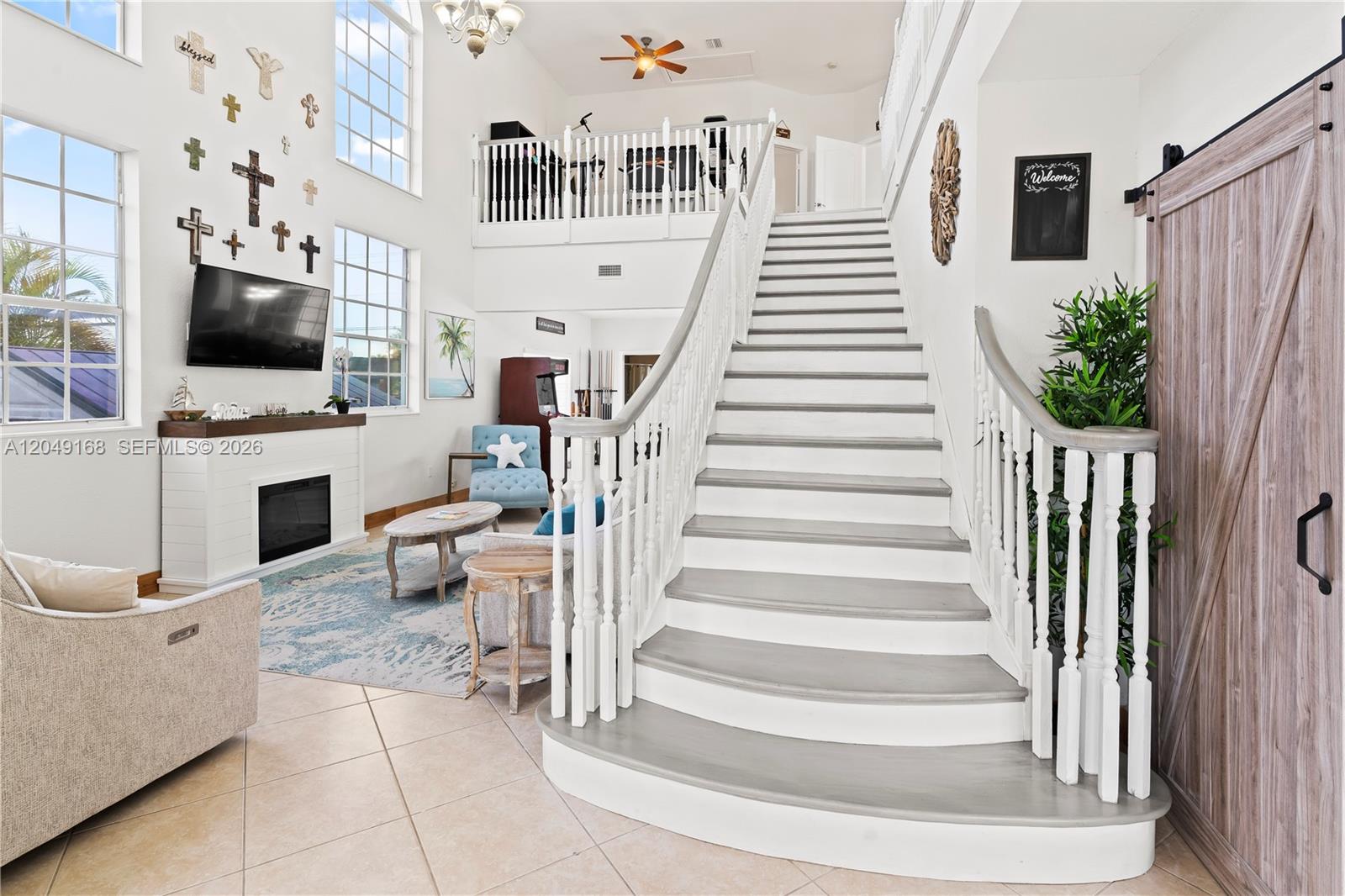 A grand staircase with white railings leads to a loft overlooking a living room — 901 Dove Ave, Miami Springs FL 33166, MIAMI SPRINGS, FL