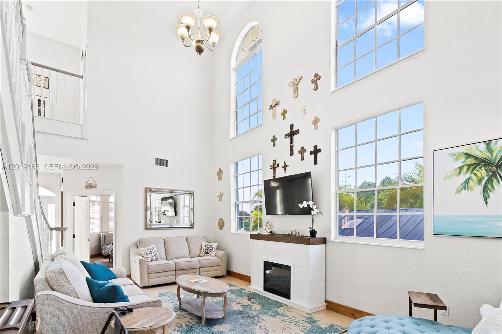 A high-ceilinged living room features a fireplace, wall-mounted television, and a collection of crosses — 901 Dove Ave, Miami Springs FL 33166, MIAMI SPRINGS, FL