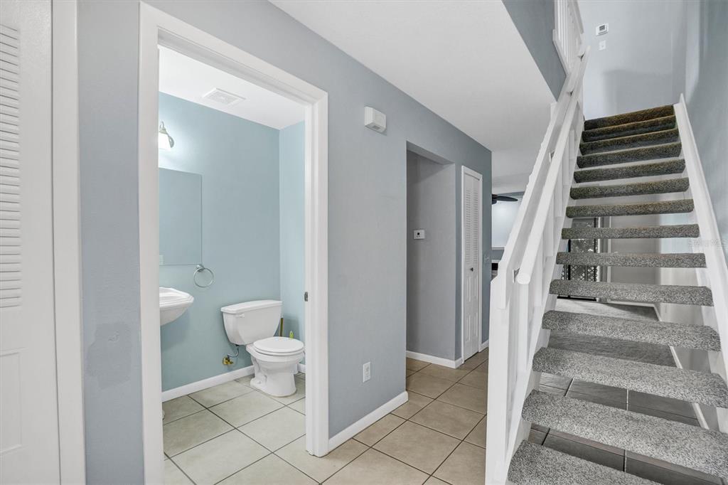 A hallway with tile flooring leads to a bathroom and a carpeted staircase with railings — 323 ORANGE BLOSSOM DRIVE UNIT 323, WINTER HAVEN, FL