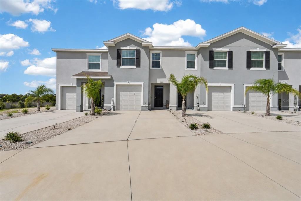 A multi-unit residential building with gray stucco siding, multiple garage doors, and a concrete driveway — 33046 MAJOR OAK DRIVE, WESLEY CHAPEL, FL