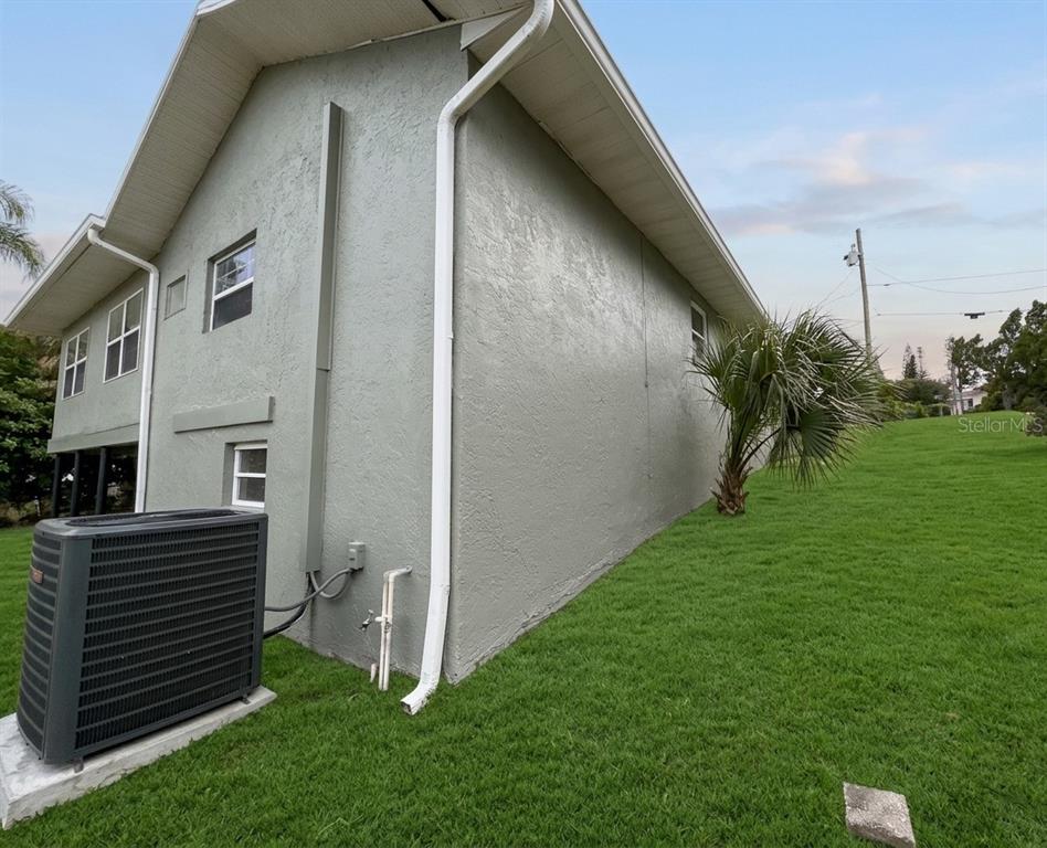 The exterior side of a gray house features a large air conditioning unit and lawn — 907 VALENTINA DRIVE, DUNDEE, FL